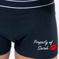 Black boxer shorts printed with an image of lips and the words property of, followed by a name